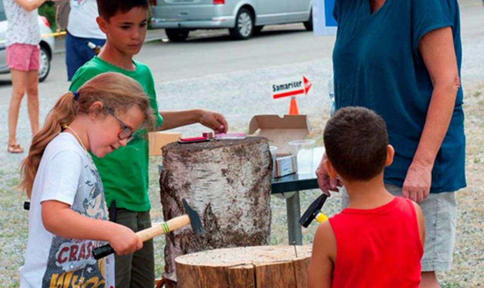 Kinder schlagen an einem Spielestand Nägel in ein Holzstück