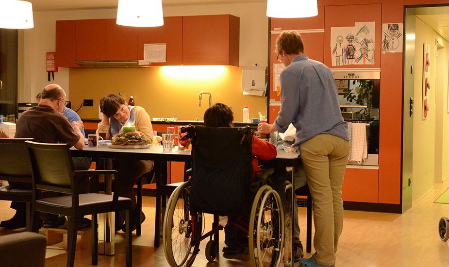 Abendessen am Küchentisch in einer Pflegewohngruppe, jemand sitzt im Rollstuhl