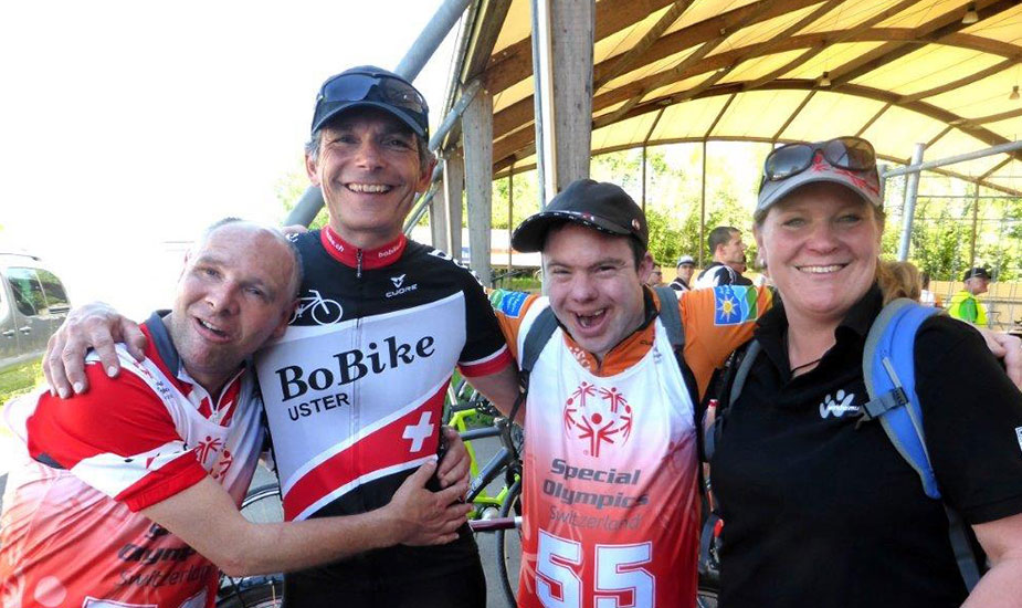 Zwei Radfahrer mit Begleitpersonen an den Special-Olymics lachen in die Kamera
